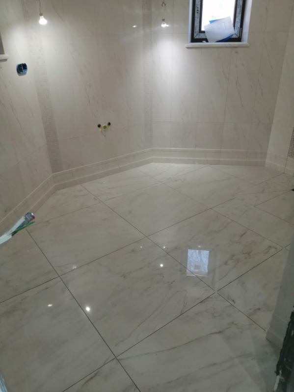 Wykończona łazienka z marmurowymi płytkami na ścianach i podłodze, ozdobnym cokołem i oknem z widocznymi materiałami budowlanymi.