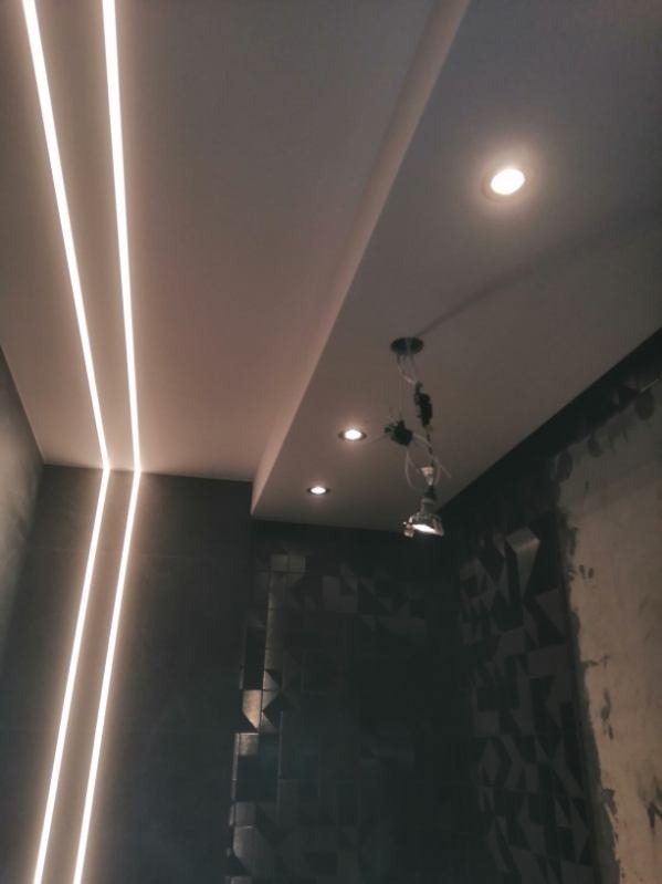 Nowoczesna łazienka w Warszawie w trakcie remontu, widoczne oświetlenie liniowe LED na suficie, punktowe lampy oraz dekoracyjna, trójwymiarowa płytka na ścianie.