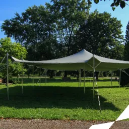 Rozłożony szary namiot plenerowy typu stretch na trawniku, z widocznymi linkami mocującymi i logo firmy w rogu zdjęcia.