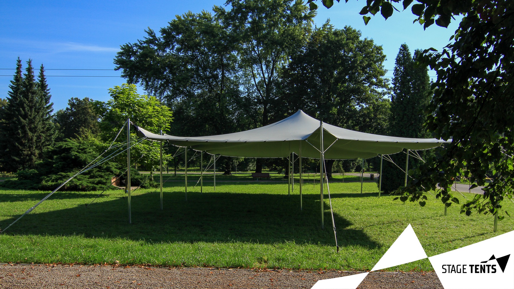 Rozłożony szary namiot plenerowy typu stretch na trawniku, z widocznymi linkami mocującymi i logo firmy w rogu zdjęcia.