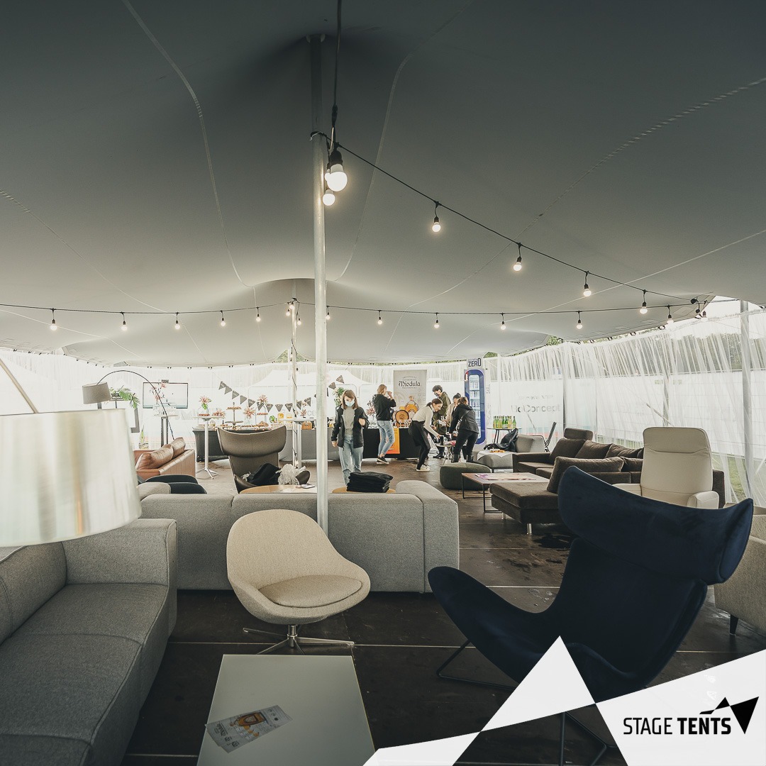 Wnętrze namiotu imprezowego z oświetleniem girlandowym, wyposażone w sofy i fotele, z widocznymi osobami w tle.