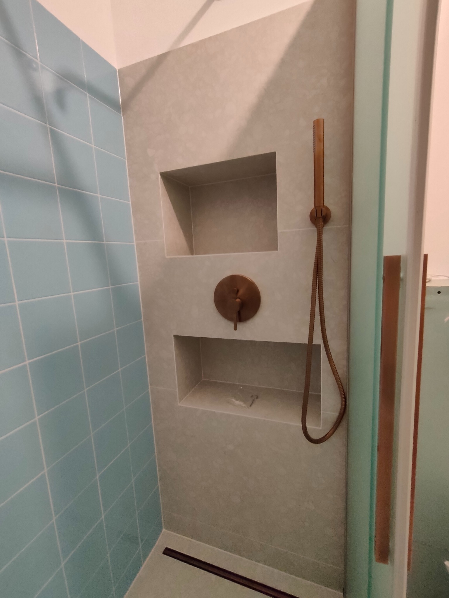 Nowoczesna kabina prysznicowa z niebieskimi płytkami, wnękami w ścianie wyłożonej szarymi płytkami i miedzianą armaturą.