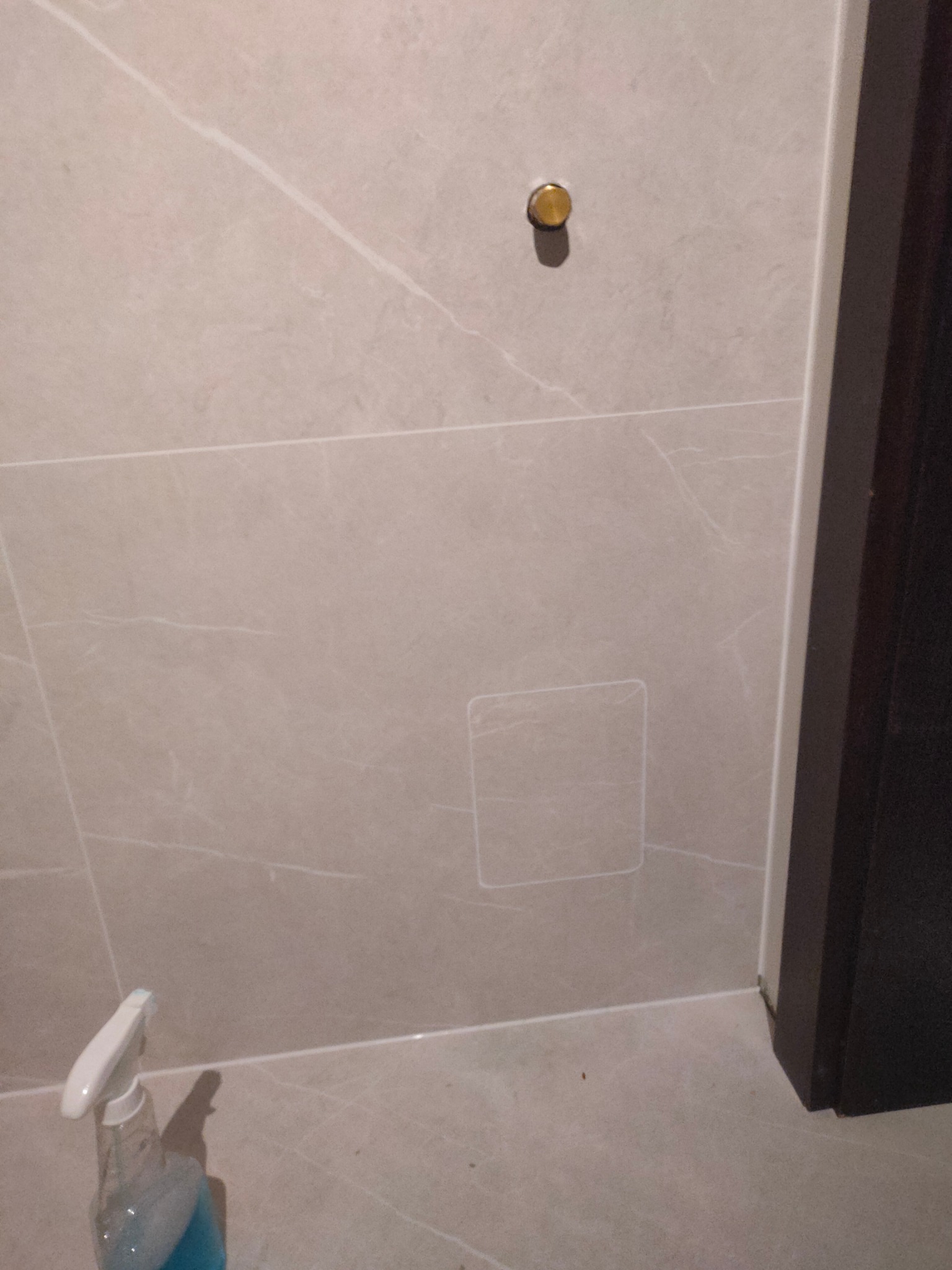 Beżowe płytki łazienkowe z delikatnym wzorem, widoczny fragment ściany z zaślepką i ślad po niedokładnie wyczyszczonej powierzchni, w rogu butelka ze środkiem czyszczącym.