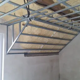 Szkielet metalowy pod płytę karton-gips na ocieplonym pianą poddaszu, widoczne przewody elektryczne i drewniane elementy konstrukcyjne.