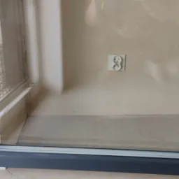 Szare okno z widocznym brudem i kurzem po remoncie, widoczny fragment ściany z gniazdkiem elektrycznym.