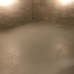 Michal Romanowicz - Surowe wnętrze piwnicy z betonowymi ścianami i świeżo wylaną, gładką, szarą posadzką. Widoczne ślady po szalunkach na ścianach i kabel zwisający z sufitu. Oświetlenie górne, ciepłe.