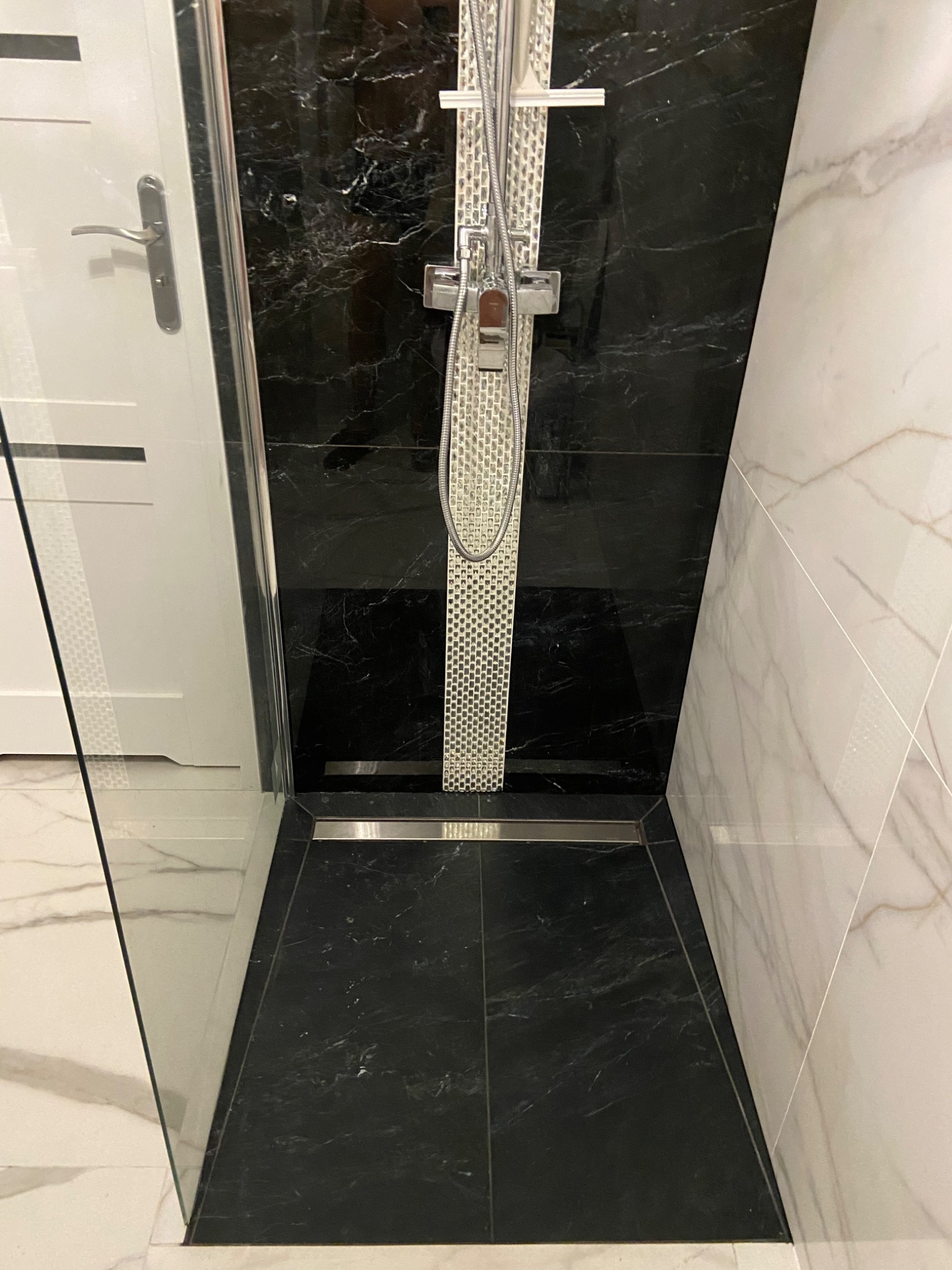 Nowoczesna kabina prysznicowa z czarnymi i białymi marmurowymi płytkami, chromowaną armaturą i odpływem liniowym.