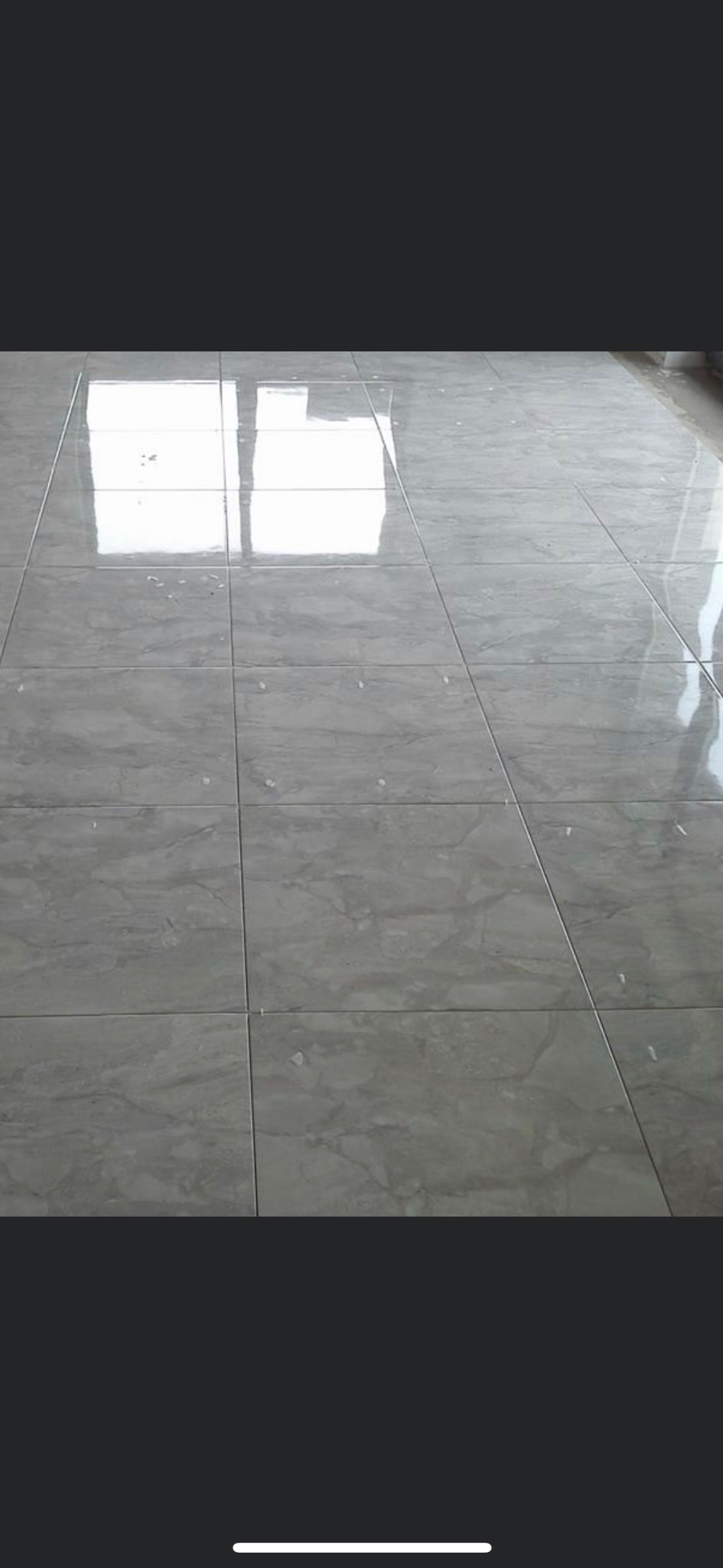 Ułożone, błyszczące, szare płytki podłogowe z widocznymi odbiciami światła i drobnymi zabrudzeniami po fugowaniu.