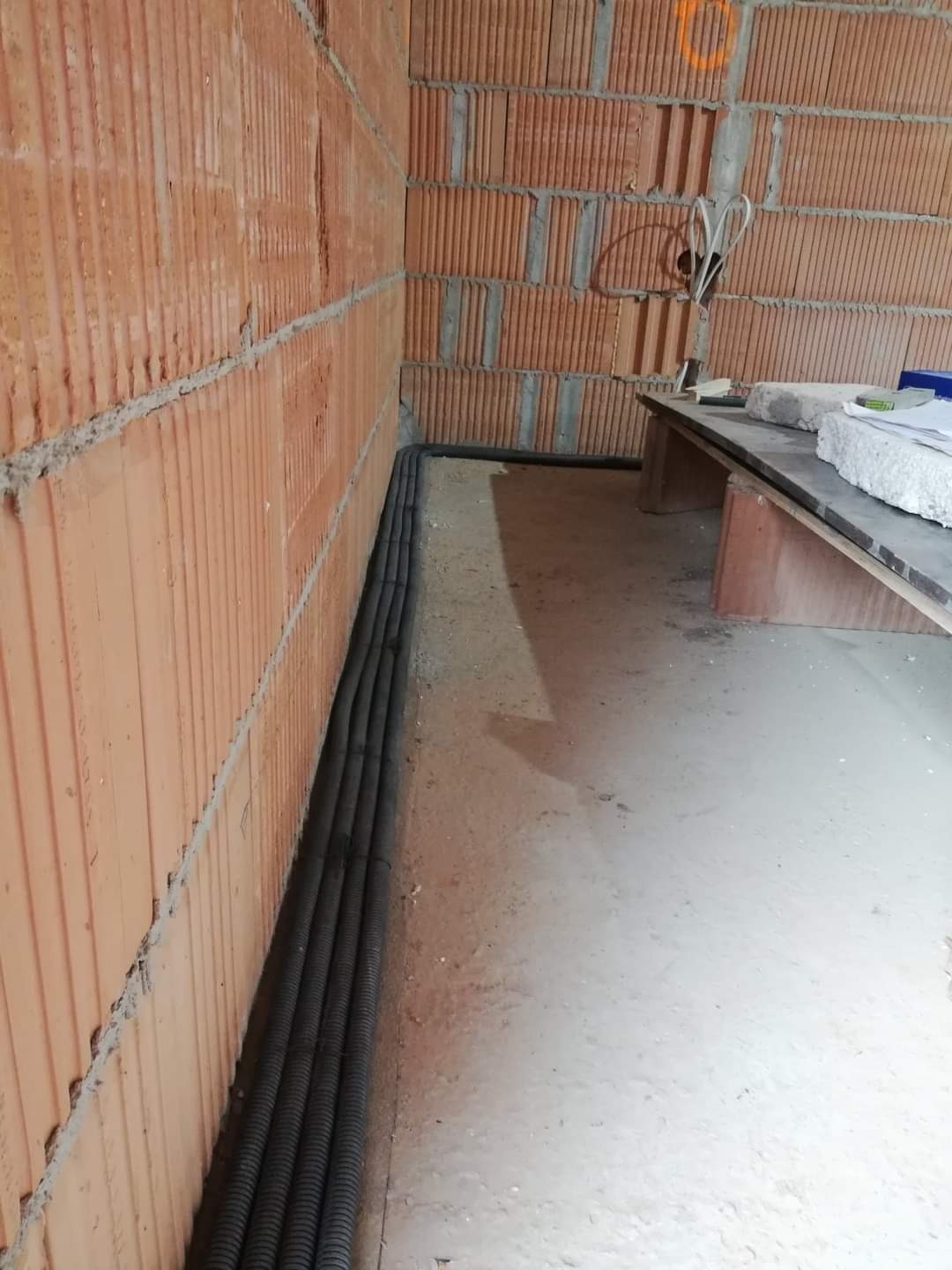 Rury ochronne kabli ułożone wzdłuż ściany z pustaków ceramicznych podczas prac budowlanych.