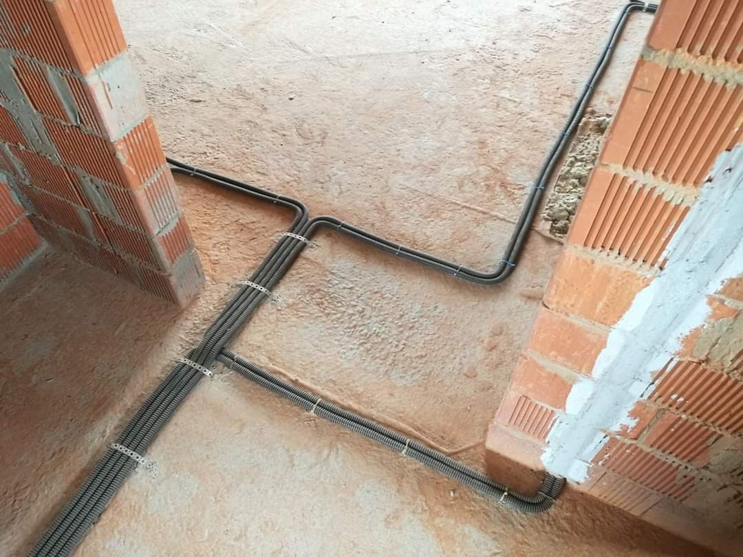 Kable elektryczne w peszlach, zamocowane do surowej podłogi i ścian z cegły dziurawki w trakcie budowy.