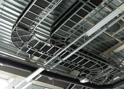 Metalowe koryta kablowe z przewodami zamontowane pod sufitem z blachy trapezowej, widoczne rury instalacyjne i oświetlenie przemysłowe.