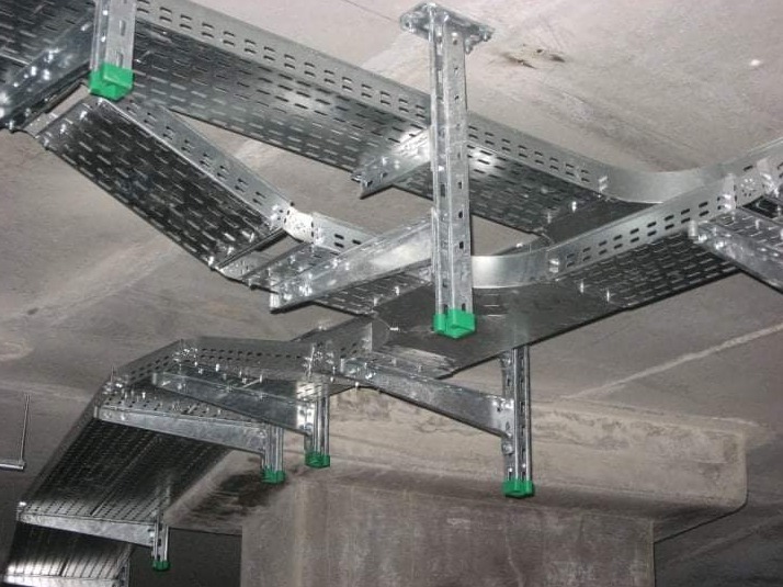 Metalowe koryta kablowe z perforacją, zamocowane pod sufitem w Katowicach, z zielonymi elementami mocującymi.