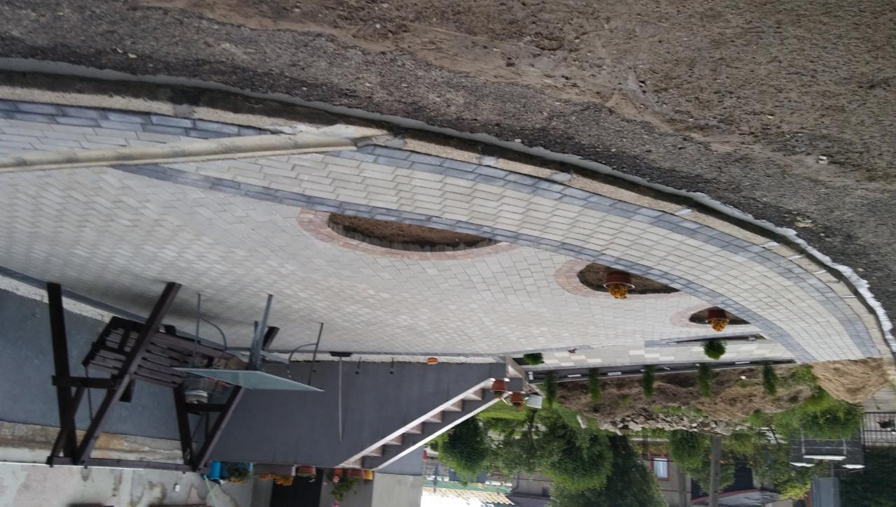 Ułożona kostka brukowa w ogrodzie z okrągłymi rabatami, widoczne krzewy i meble ogrodowe.