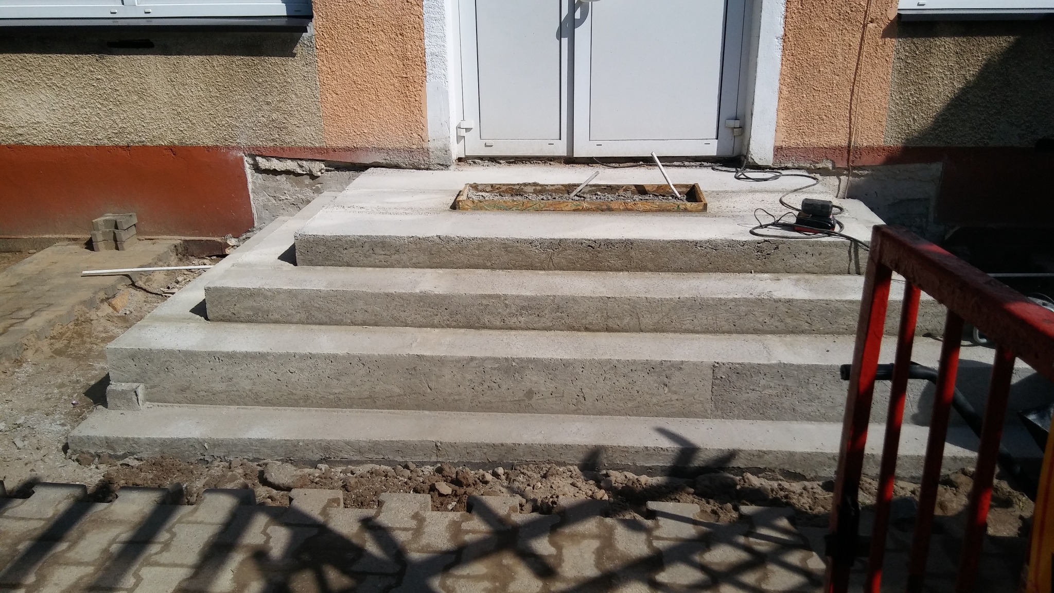 Wykonywane betonowe schody wejściowe do budynku w miejscowości Dobra, widoczne elementy szalunku i podłączenie elektryczne do narzędzi.