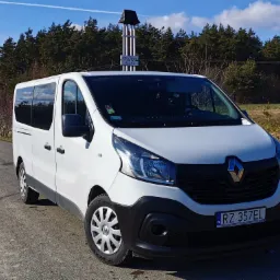 Biały bus Renault Trafic na bocznej drodze z widokiem na las i drogowskaz miejscowości Pruchnik Żegna