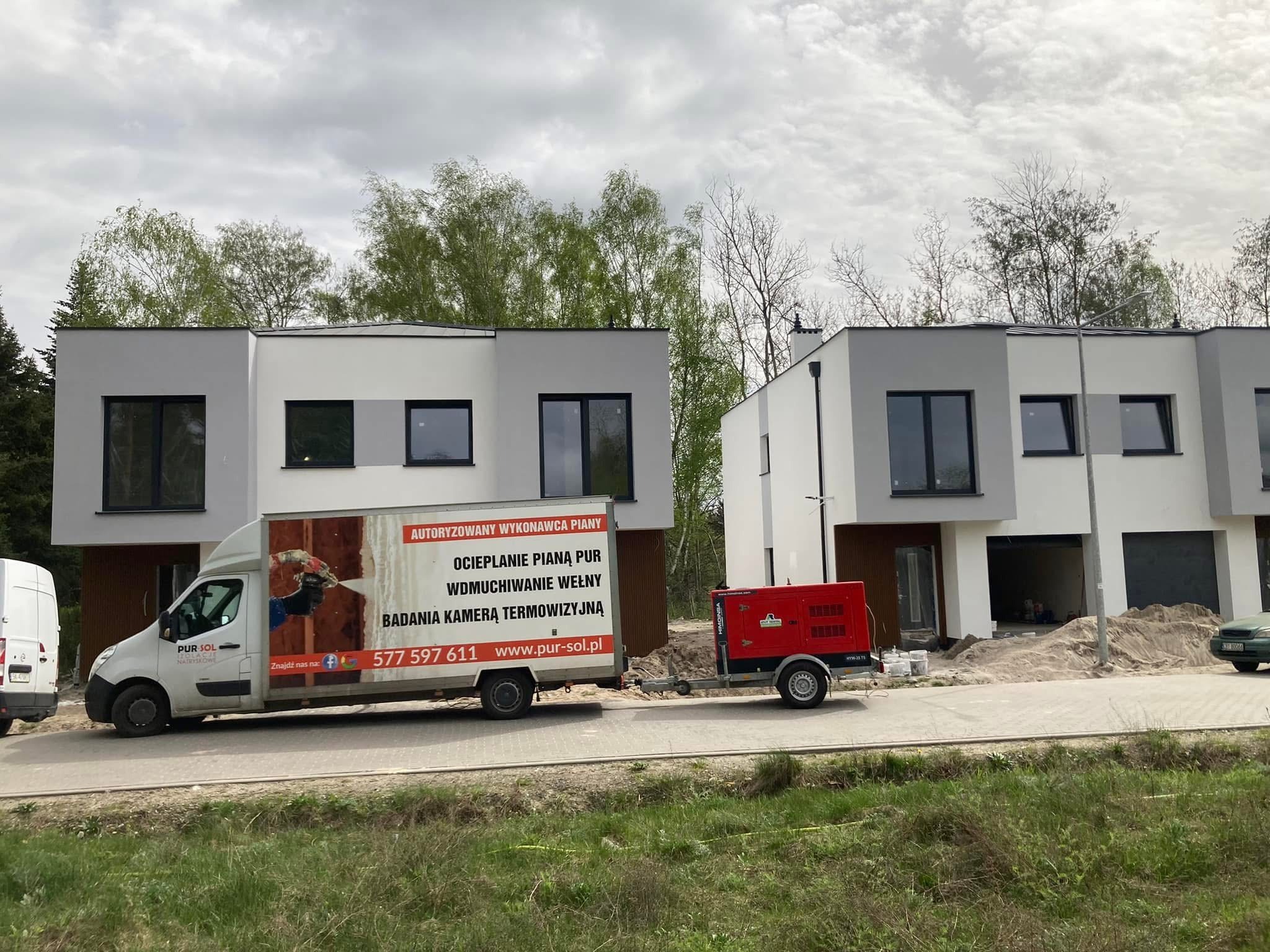 Ocieplanie pianą PUR: zabudowa szeregowa w trakcie izolacji. Na pierwszym planie samochód dostawczy z reklamą firmy i agregat prądotwórczy. Widok z zewnątrz.
