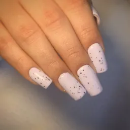 Delikatny manicure z jasnoróżowym lakierem i czarnymi, drobnymi kropeczkami na kwadratowych paznokciach.
