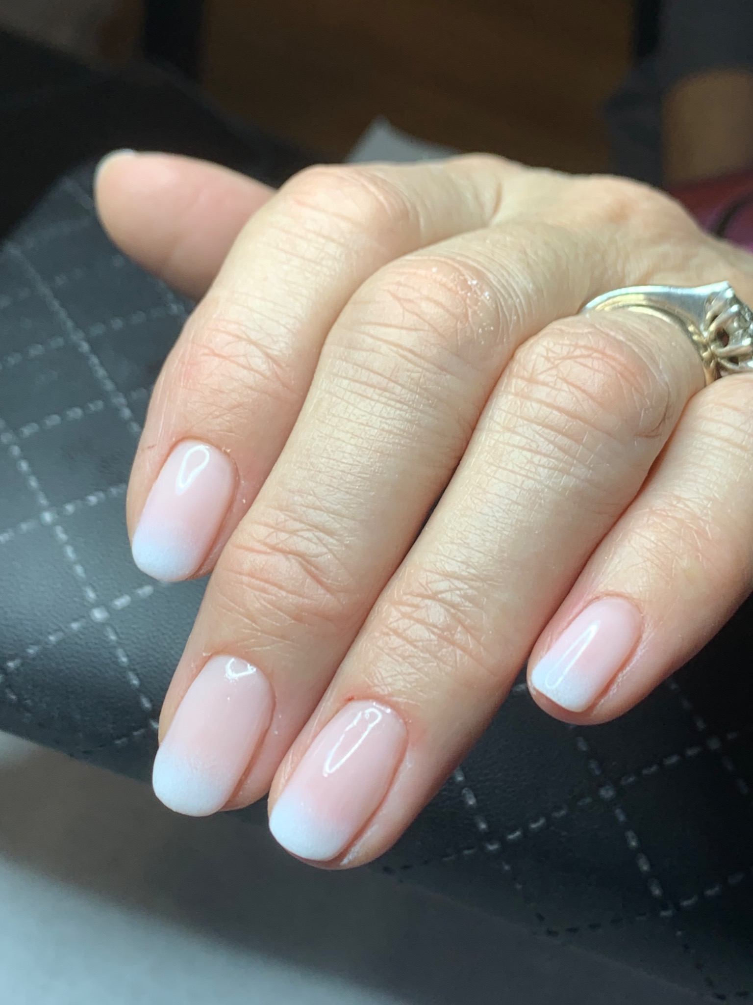 Dłoń z delikatnym, ombre manicure w odcieniach różu i bieli, ozdobiona srebrnym pierścionkiem z ornamentem.