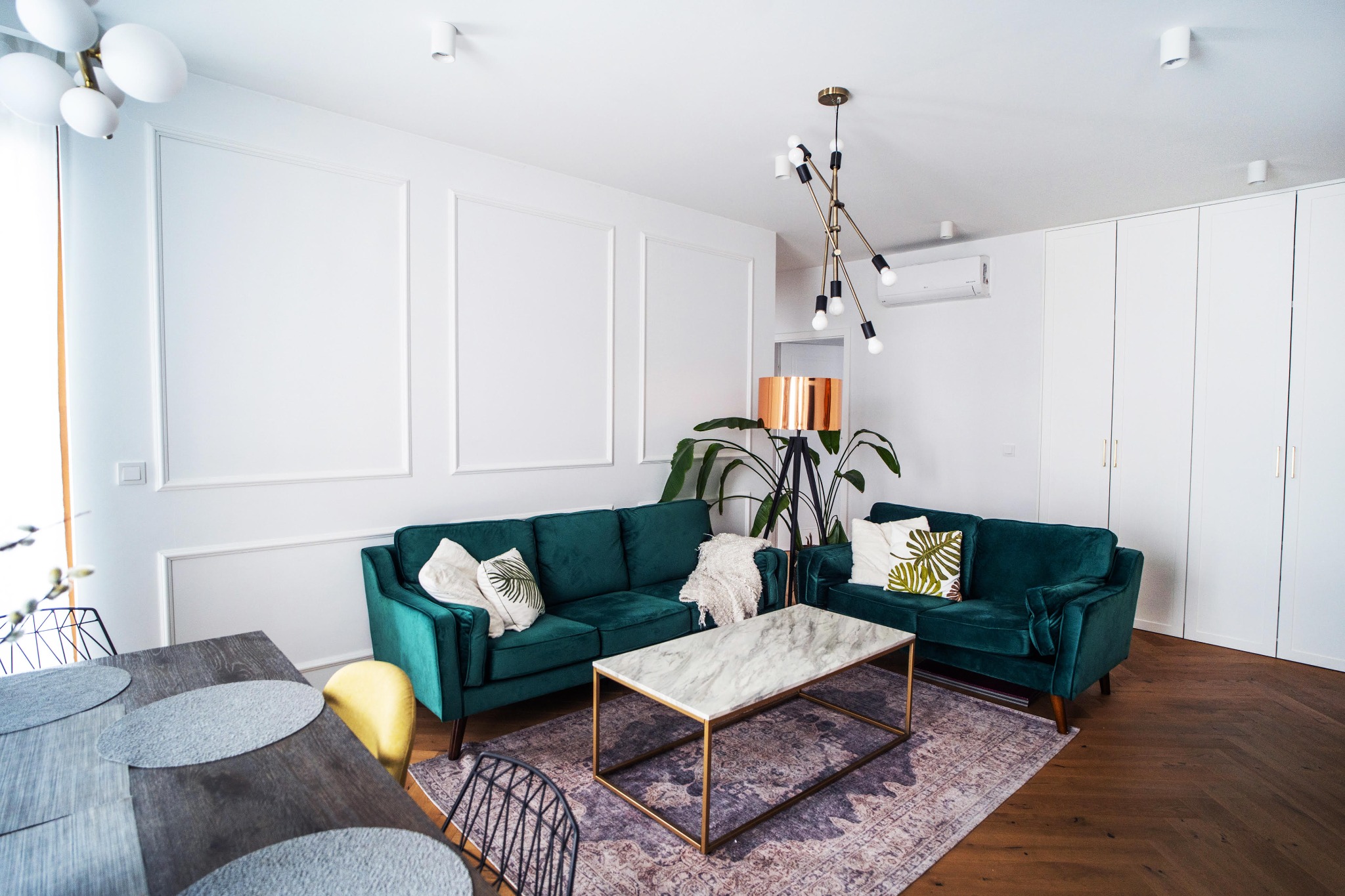 Nowoczesny salon z zieloną sofą, marmurowym stolikiem kawowym i drewnianą podłogą w jodełkę, oświetlony lampą w stylu mid-century modern i lampą podłogową z miedzianym abażurem.