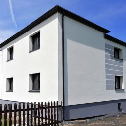 Zakład Budowlany Mandrysz Bronisław - Dwukondygnacyjny dom po remoncie elewacji, z białymi ścianami i grafitowymi detalami, widoczny fragment ogrodzenia i pracownik w tle.