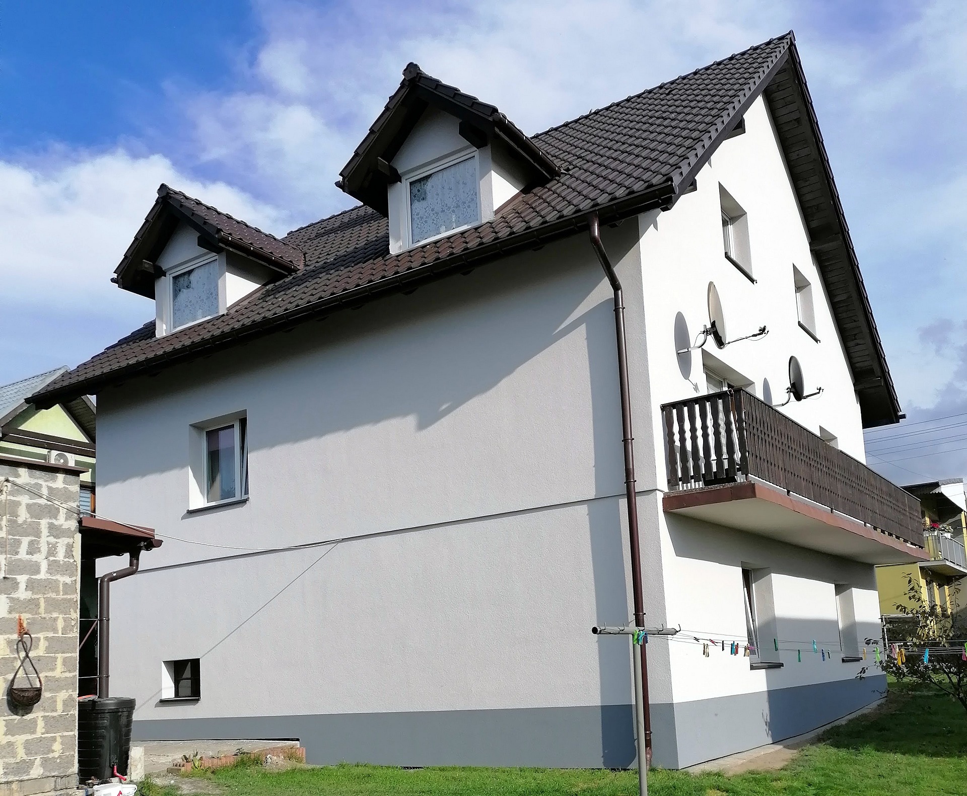Dwukondygnacyjny dom z balkonem po renowacji elewacji, widoczne anteny satelitarne i suszarka na pranie.