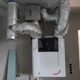 Wnętrze w trakcie remontu z zamontowaną centralą wentylacyjną Zehnder ComfoAir Q, z podłączonymi przewodami wentylacyjnymi w srebrnej izolacji oraz skrzynką rozprężną IZZIFAST.