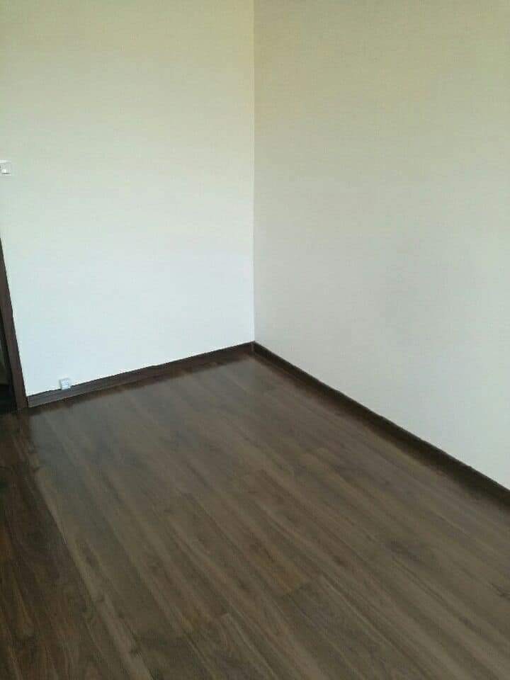 Wnętrze pokoju po remoncie: ściany pomalowane na jasny odcień, ciemna, lakierowana podłoga z paneli oraz listwy przypodłogowe.