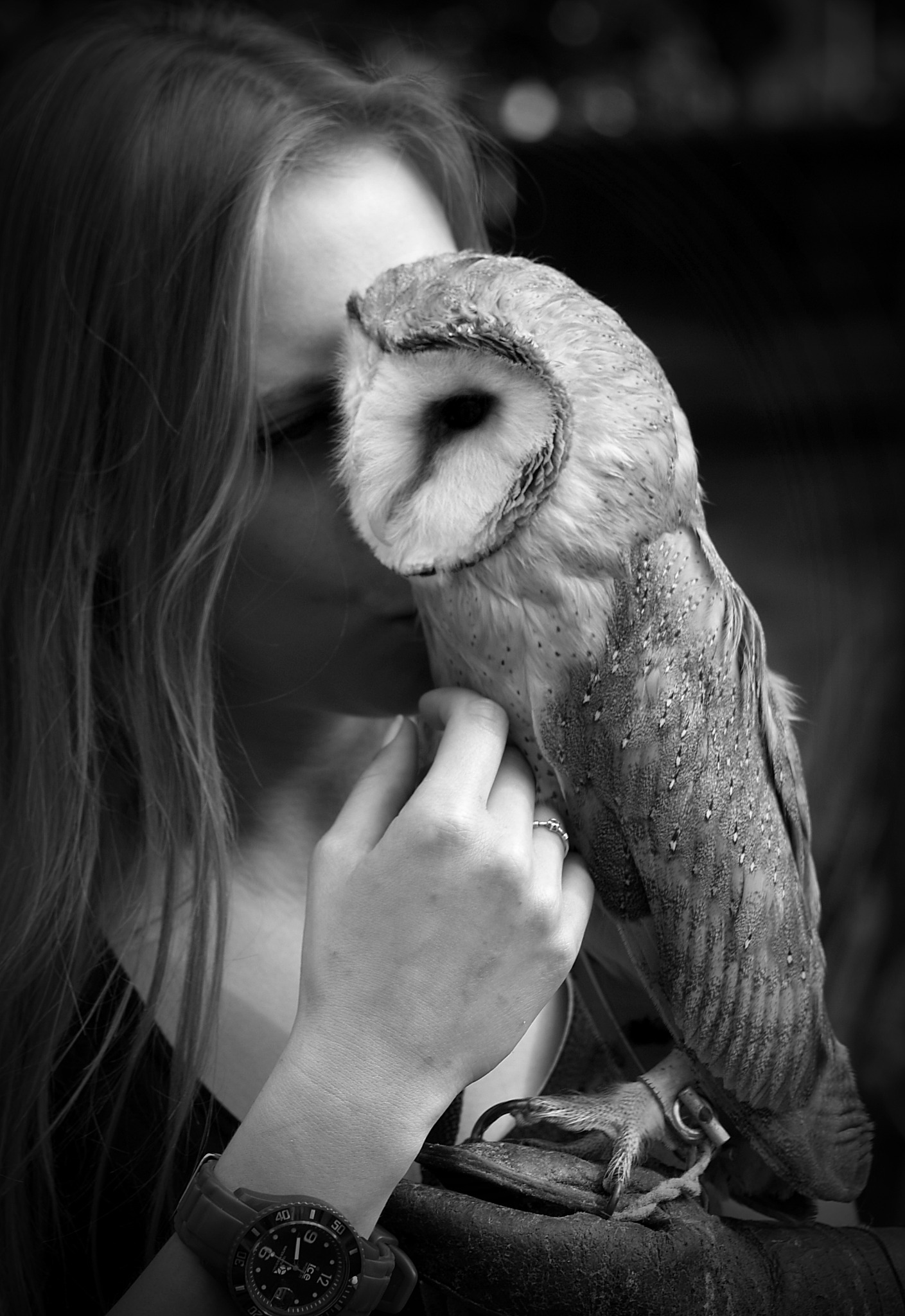 Portret kobiety z sową płomykówką trzymaną na rękawicy, czarno-białe zdjęcie z widocznym zegarkiem na nadgarstku.