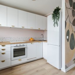 AKORD Volodymyr Rushchak - Nowoczesna kuchnia w bieli z drewnianym blatem, mozaikową ścianą nad blatem, złotymi uchwytami i dekoracyjną tapetą w roślinne wzory na ścianie bocznej.
