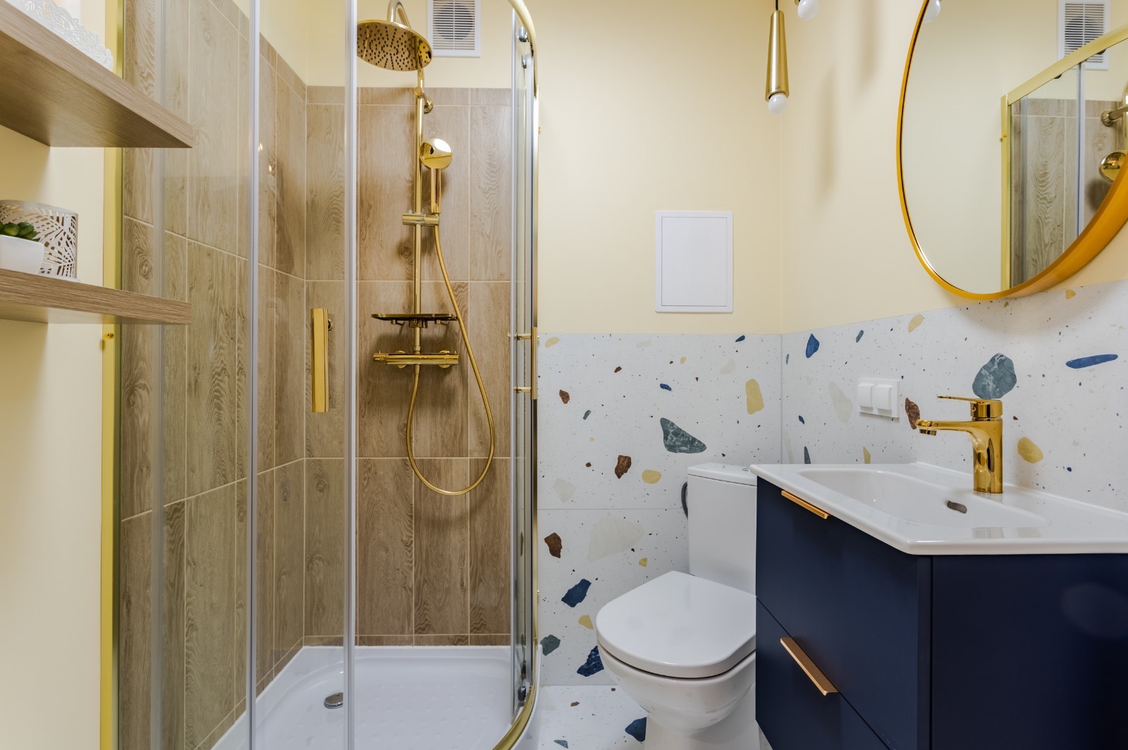 Nowoczesna łazienka z kabiną prysznicową, złotą armaturą i umywalką z szafką w kolorze granatowym, wykończona płytkami w stylu lastryko.