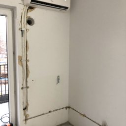 BestAir4You. ALBERT BAREJA - Nowoczesny klimatyzator ścienny zamontowany nad oknem, widoczne kable i rury prowadzone po ścianie w trakcie montażu, ślady po kuciu w ścianie.