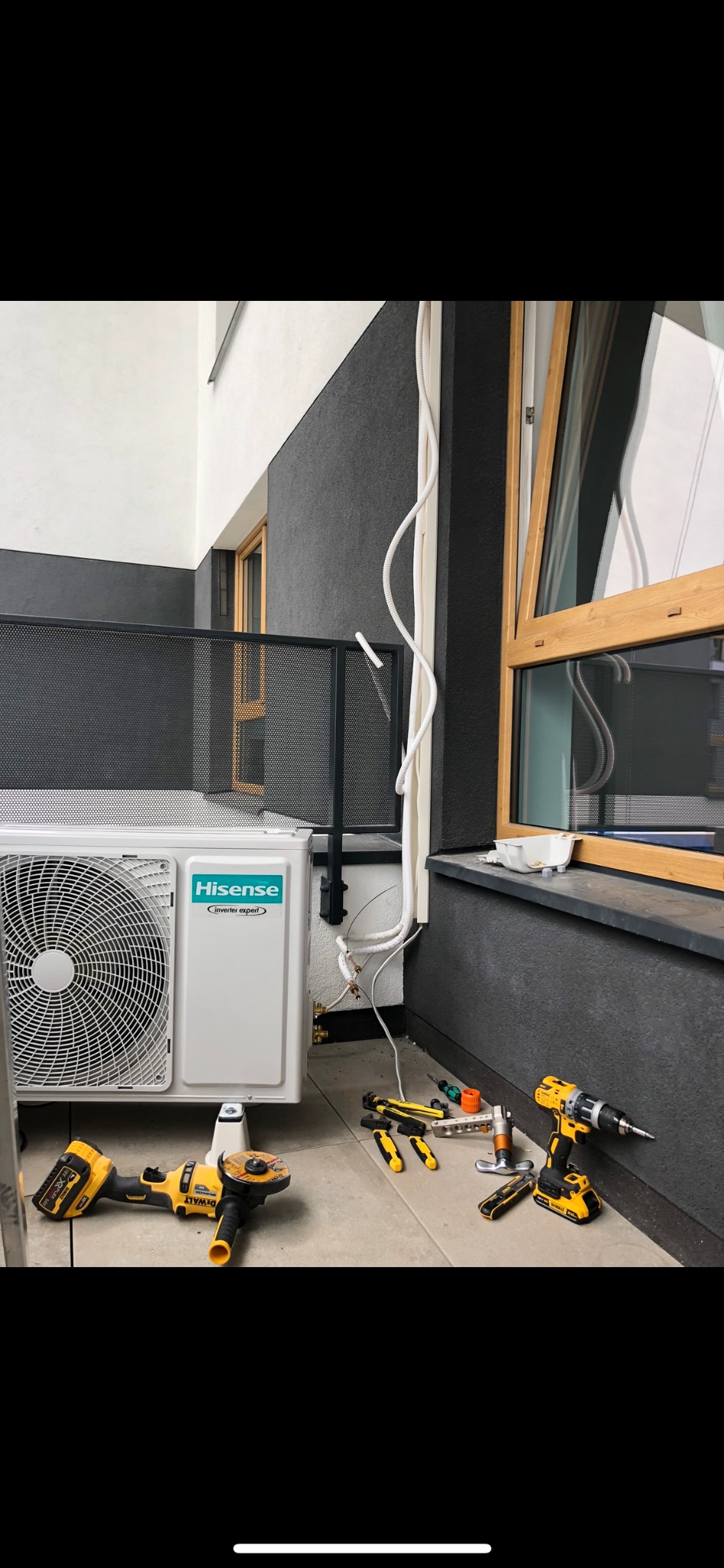 Zewnętrzna jednostka klimatyzacji marki Hisense zamontowana na balkonie, obok widoczne narzędzia: szlifierka kątowa DeWalt, wiertarka DeWalt, kombinerki, klucze, obcinak do rur, kształtki miedziane...