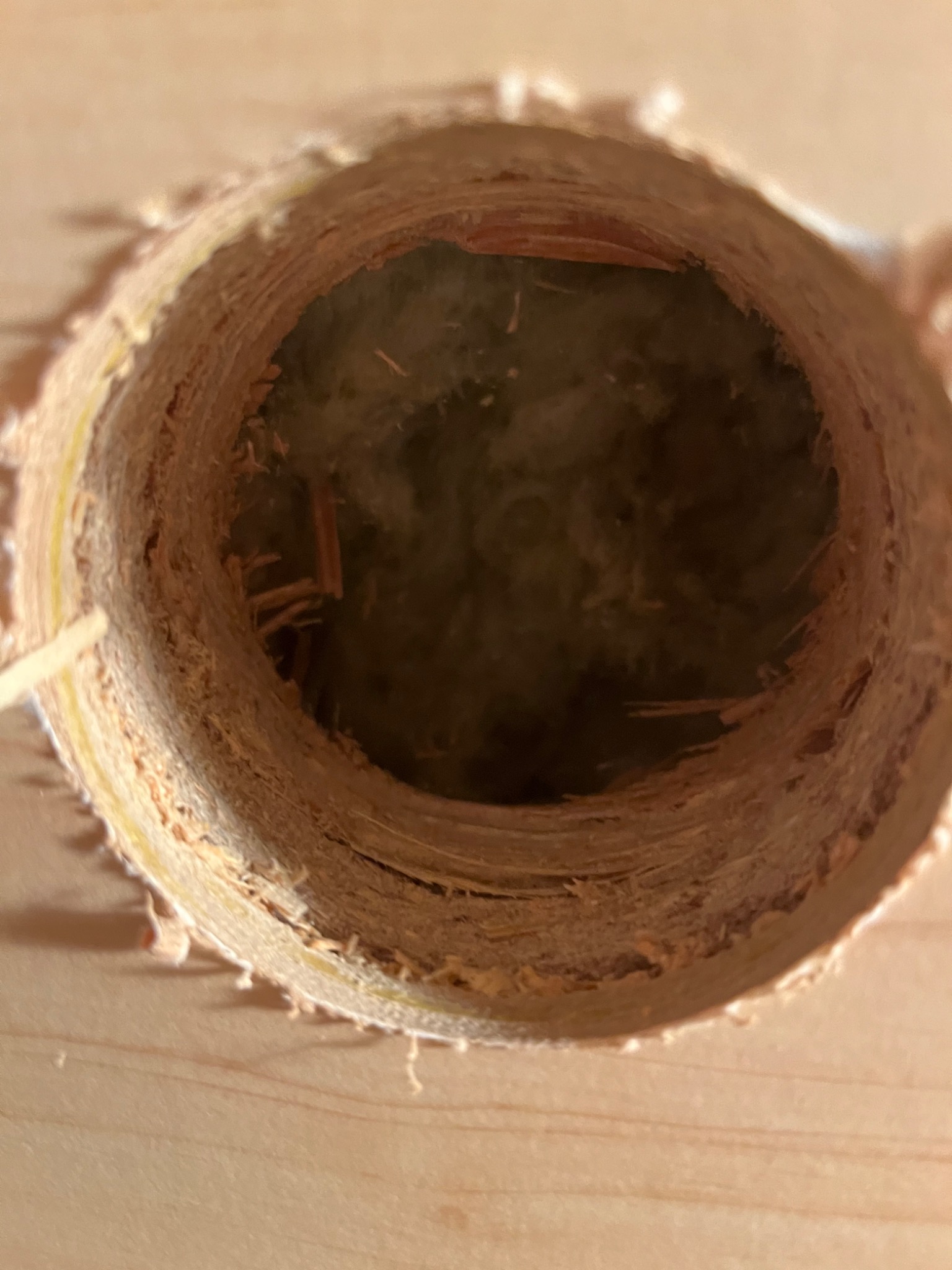 Otwór w ścianie z widoczną izolacją w środku, świeżo wywiercony, z widocznymi wiórami i nierównościami.