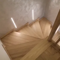 Kątowe ujęcie dębowych schodów z oświetleniem LED w ścianie i minimalistyczną balustradą, widok z góry.