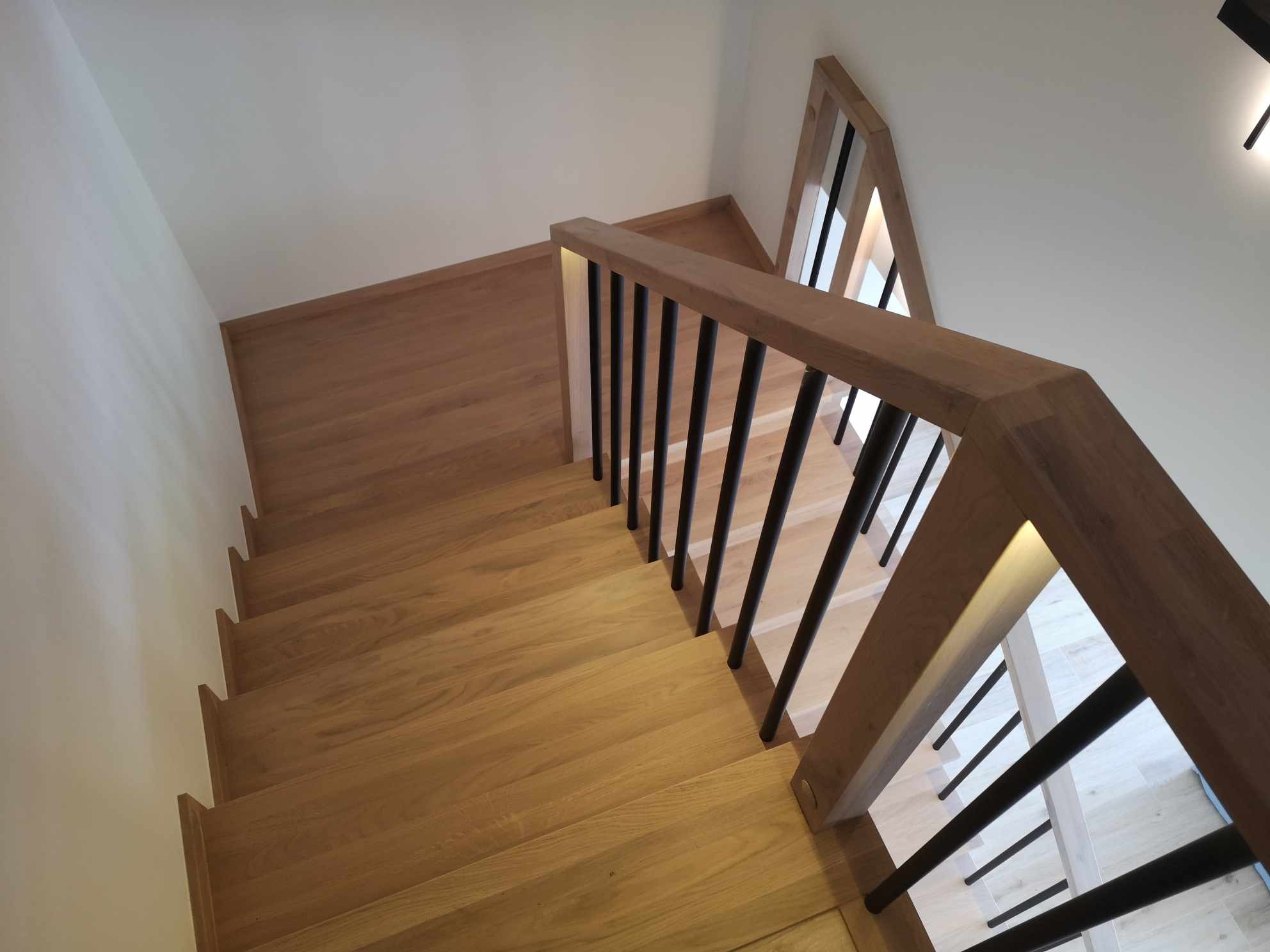 Nowoczesne schody z jasnego drewna z czarnymi metalowymi balustradami, oświetlenie LED zintegrowane z poręczą, widok z góry.