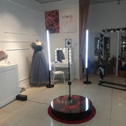 Oświetlona platforma obrotowa z telefonem, otoczona lampami LED, w tle manekin w długiej sukni, toaletka z lustrem i dekoracje.