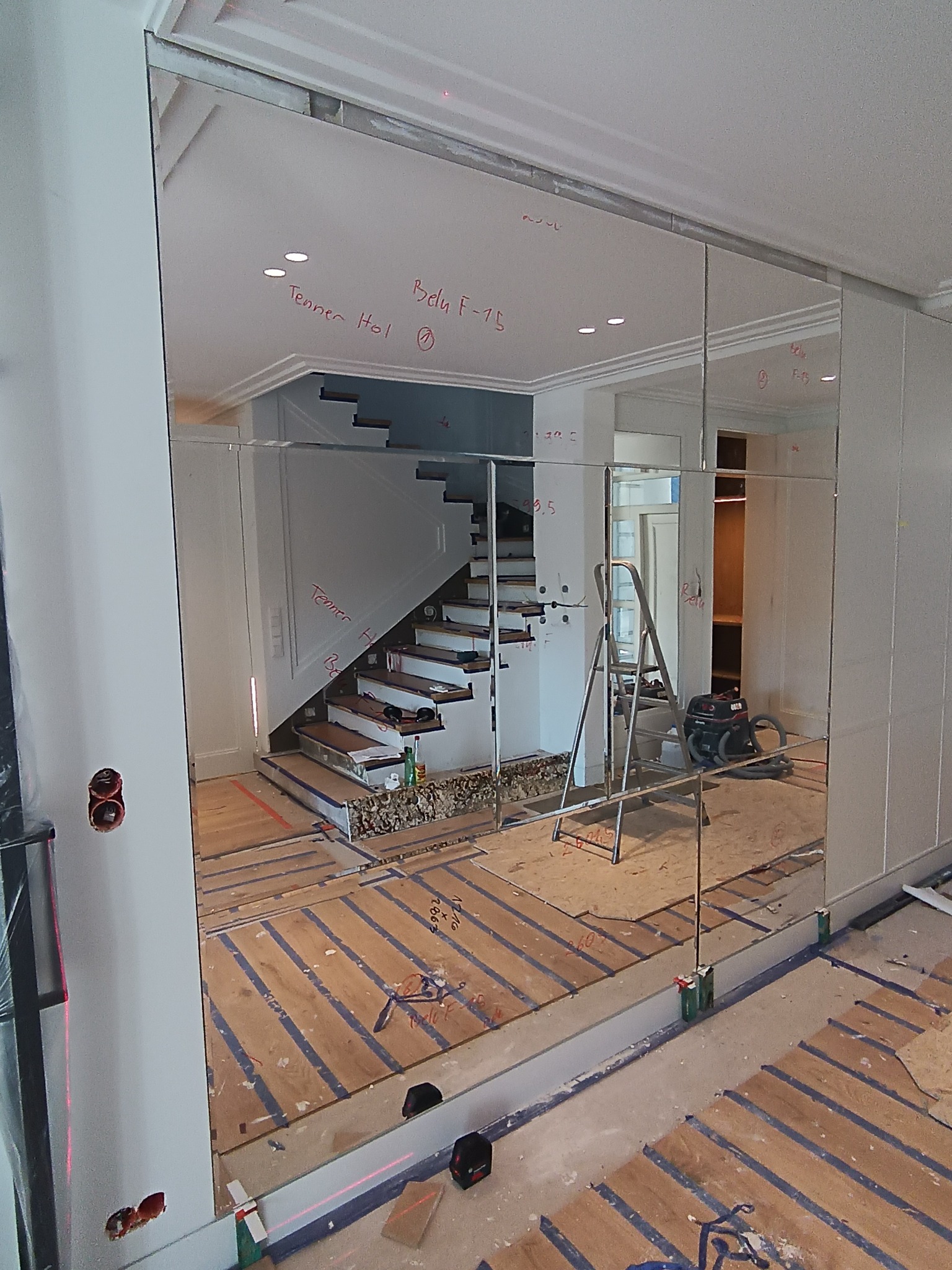 Montaż lustrzanej ściany w holu z widocznymi śladami pomiarów laserowych, schodami w tle i elementami wykończeniowymi podłogi.