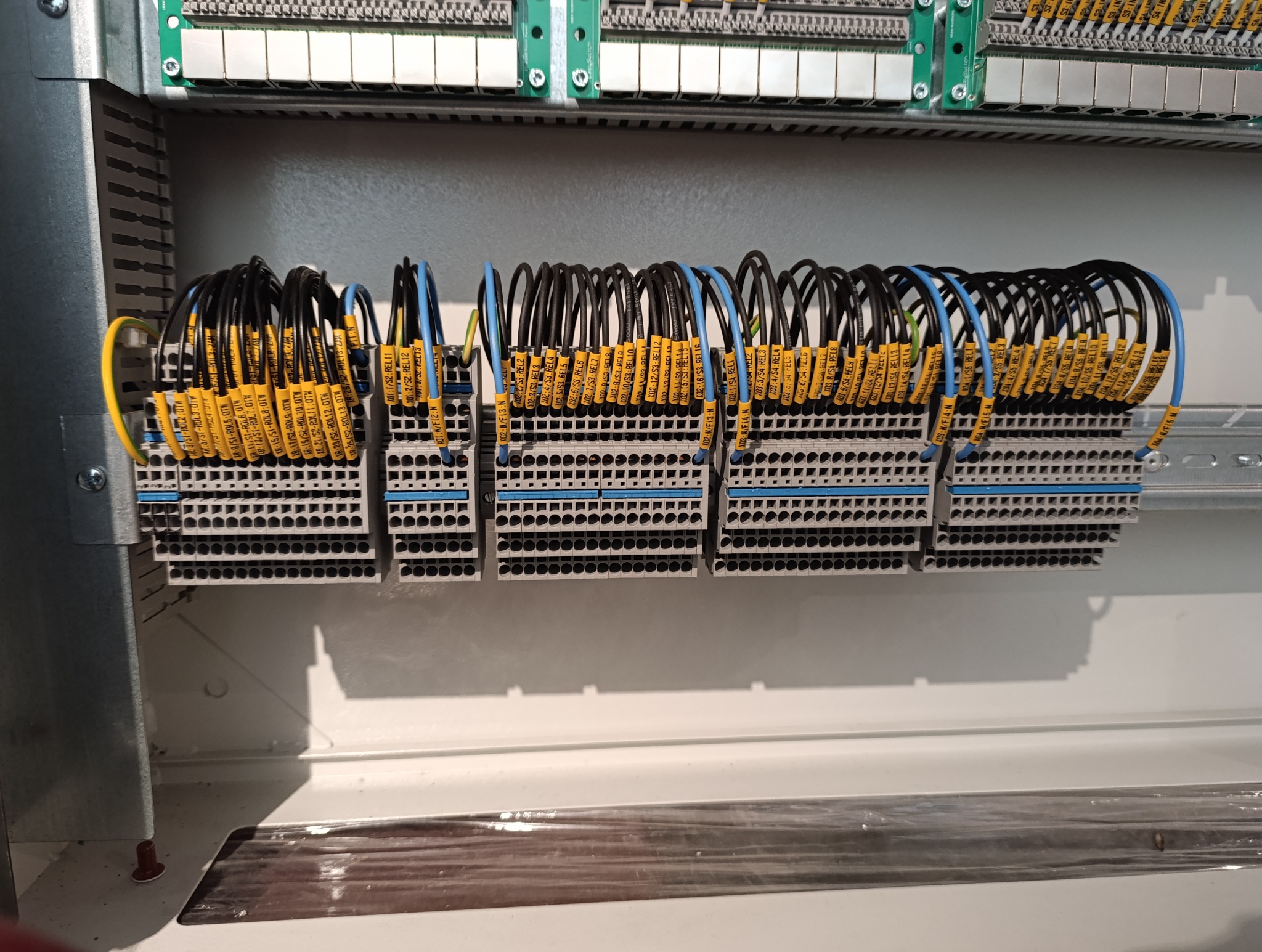 Szczegółowe ujęcie panelu sterowniczego z podłączonymi przewodami oznaczonymi żółtymi etykietami w Imielinie, widoczne szyny DIN i listwy zaciskowe.