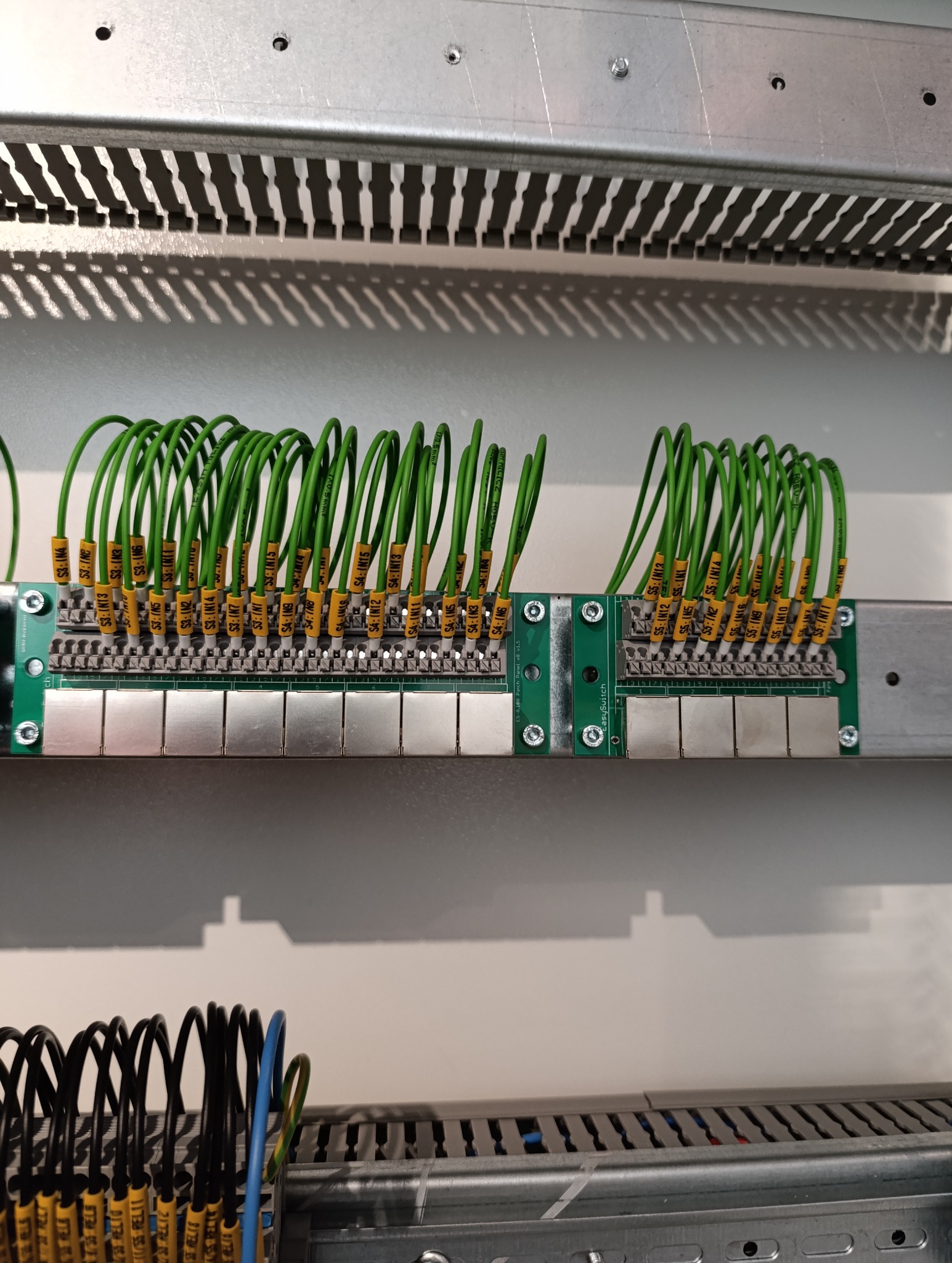 Szyna DIN z podłączonymi przewodami elektrycznymi oznaczonymi żółtymi etykietami, widoczne złącza i moduły elektroniki w szafie sterowniczej