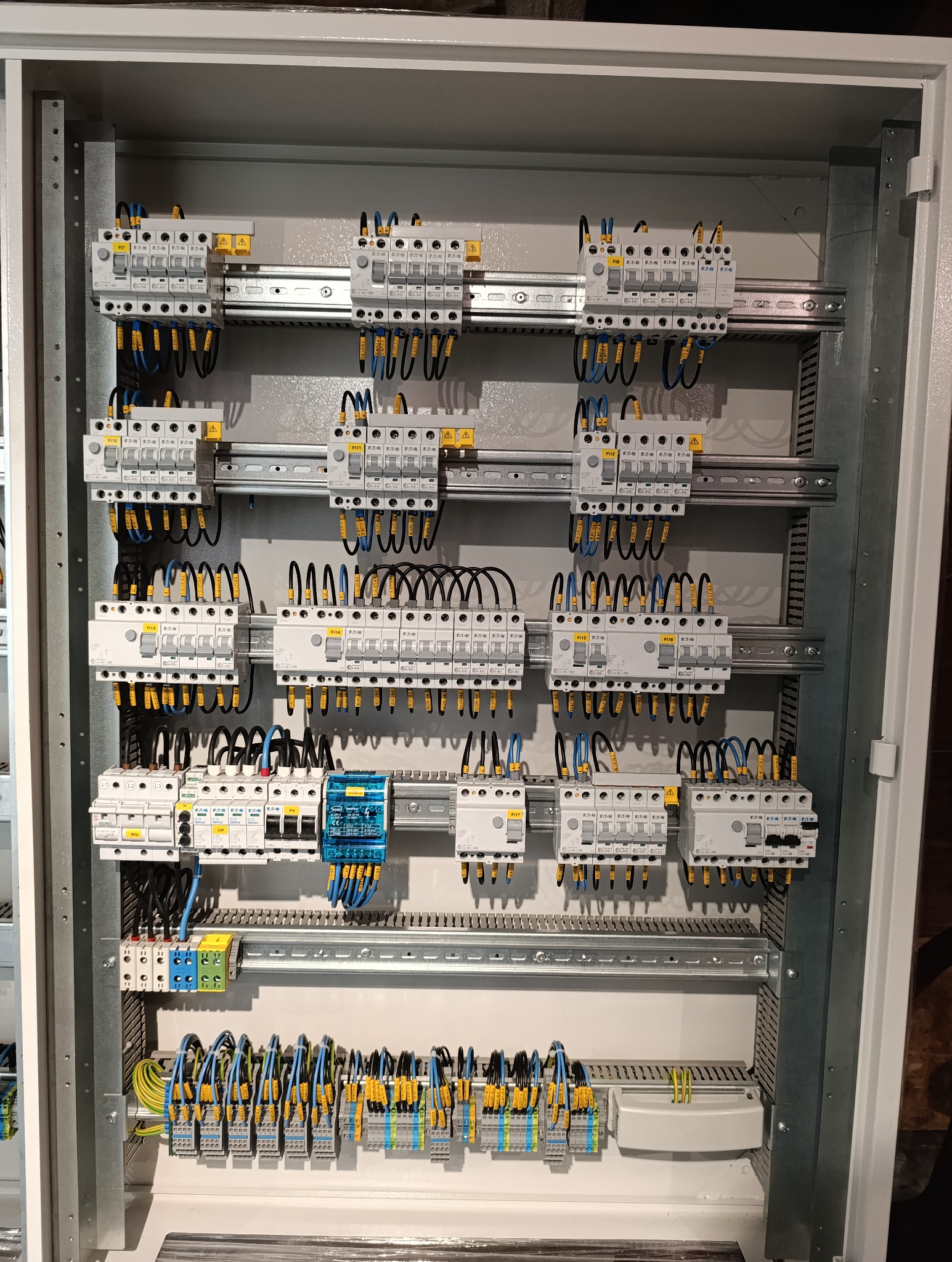 Rozdzielnica elektryczna z zamontowanymi bezpiecznikami i okablowaniem, widoczne oznaczenia na przewodach i elementach, zainstalowane na szynach DIN wewnątrz metalowej obudowy.