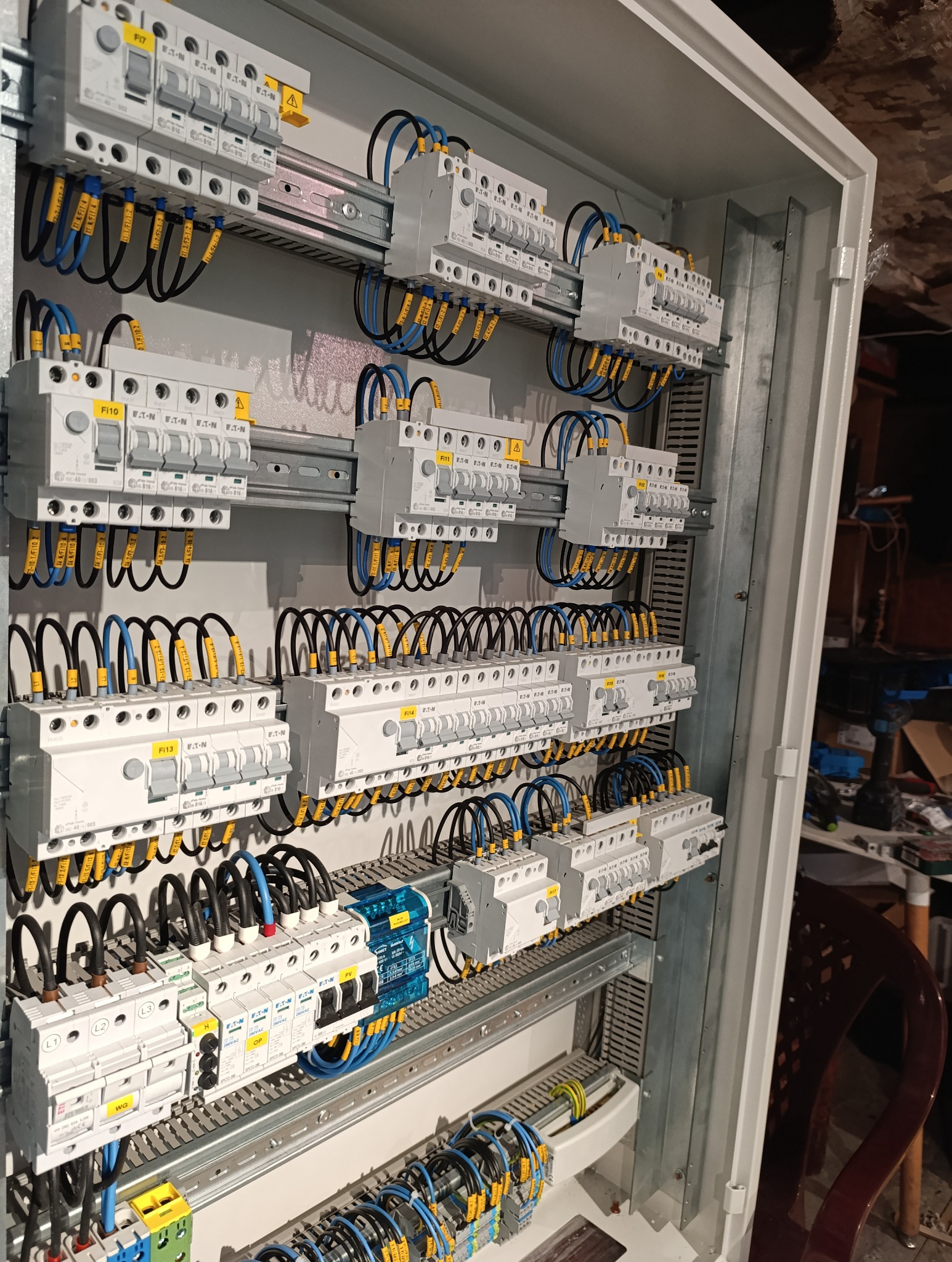 Rozdzielnica elektryczna z zamontowanymi bezpiecznikami i okablowaniem, przewody oznaczone żółtymi etykietami, widoczne elementy automatyki zabezpieczeniowej.