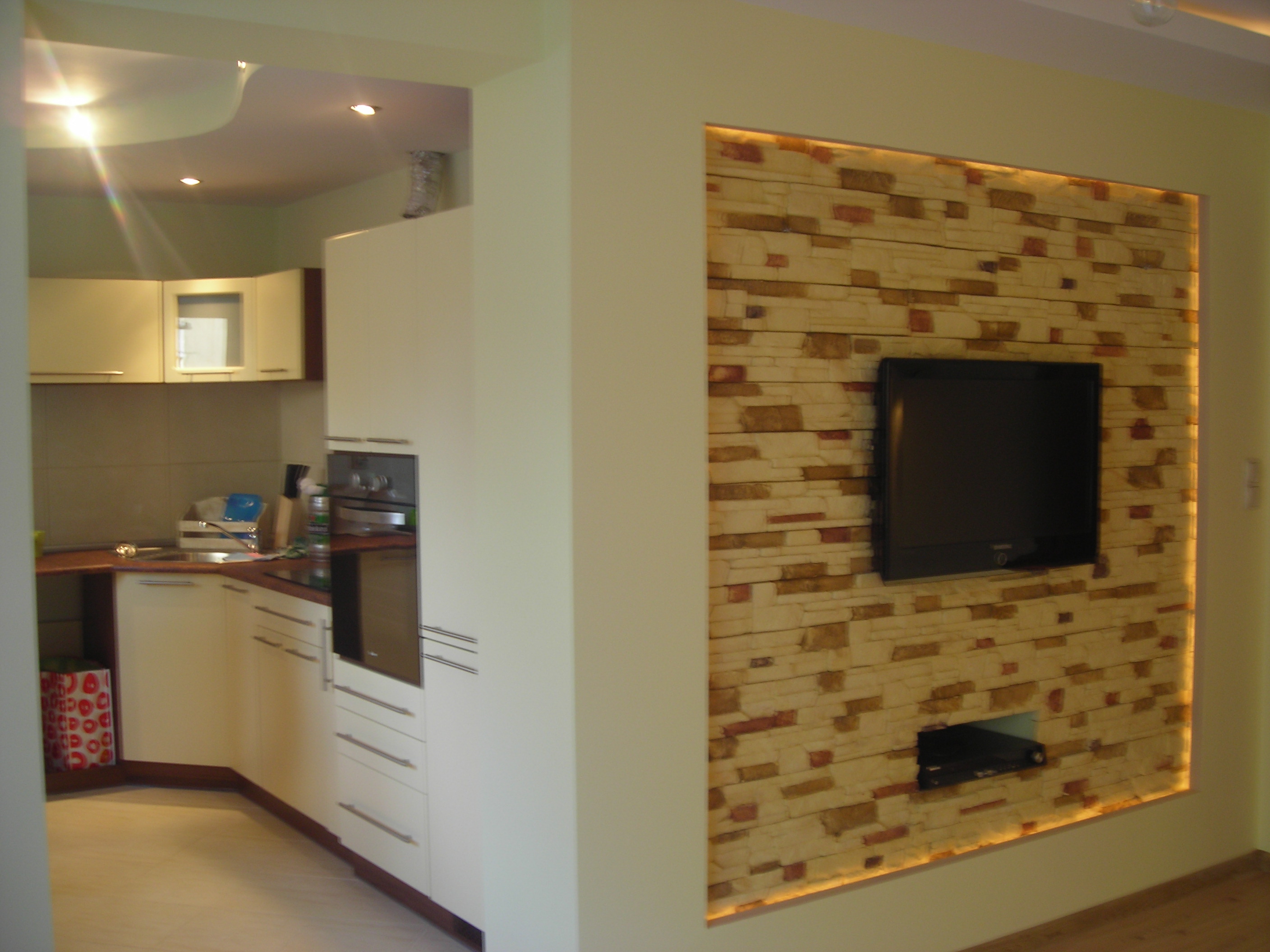Wykończona kuchnia z nowoczesnym panelem ściennym imitującym kamień, podświetlonym od tyłu, z zamontowanym telewizorem i odtwarzaczem DVD.