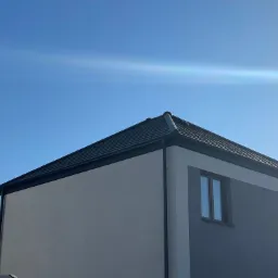 Nowoczesny dom z ciemnoszarą dachówką i dwukolorową elewacją w odcieniach szarości, widok z dołu w słoneczny dzień.