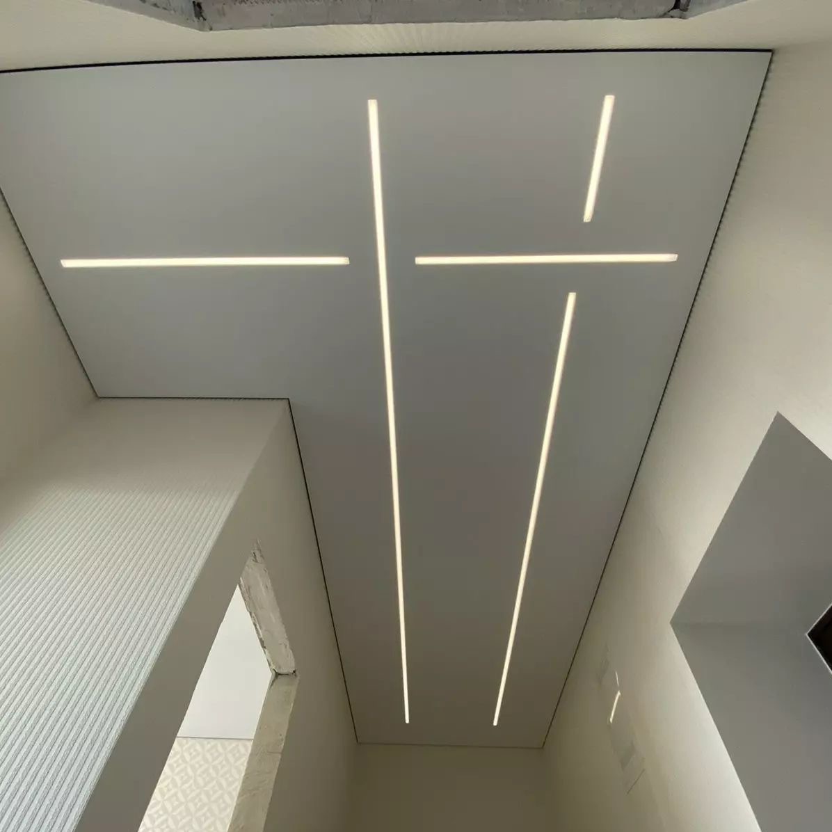 Geometryczny biały sufit z wbudowanymi liniami LED, widok z dołu, minimalistyczne wnętrze.
