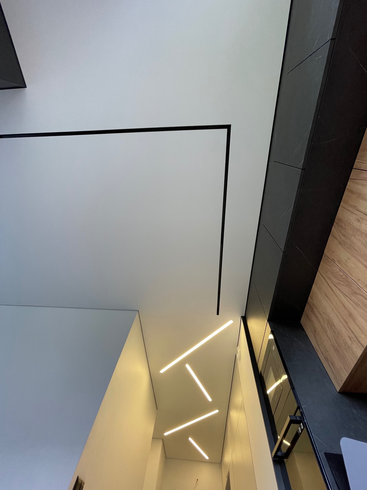 Biały sufit napinany z czarnymi, geometrycznymi liniami i nowoczesnym oświetleniem LED w formie prostych pasków, widok z dołu.