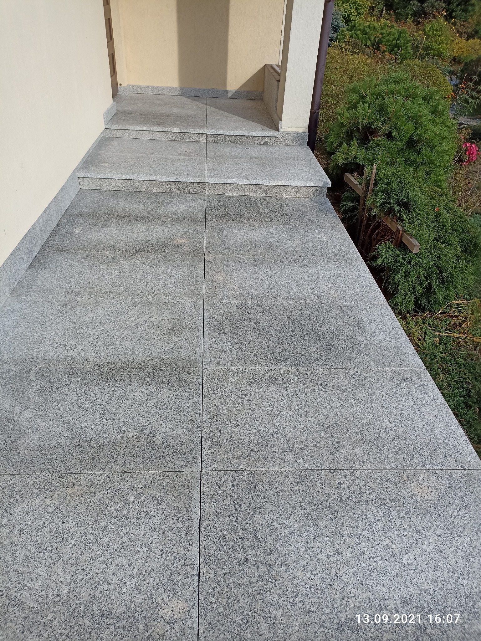 Granitowe płytki na schodach wejściowych i chodniku, widok z góry, z datą na dole po prawej stronie.