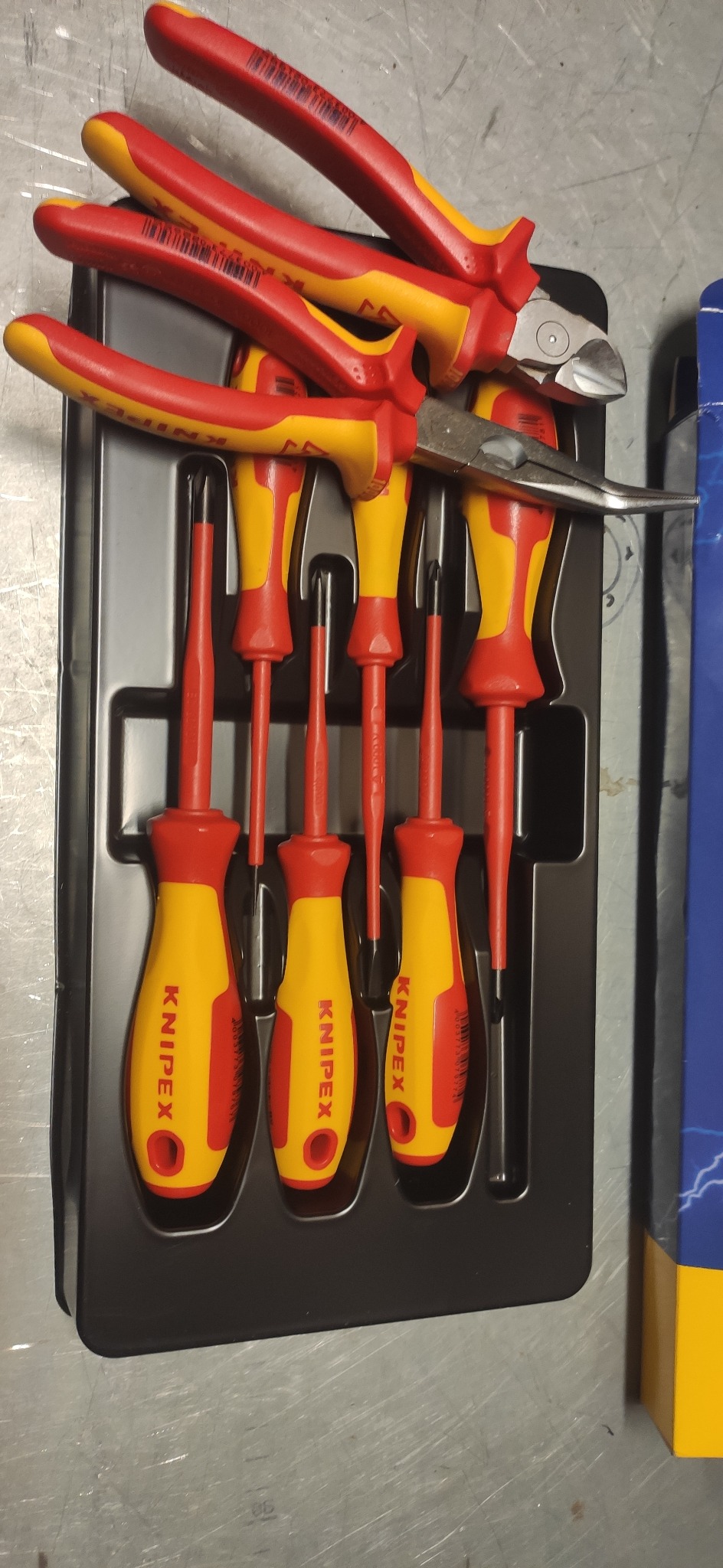 Zestaw izolowanych narzędzi Knipex: szczypce tnące, kombinerki i wkrętaki, umieszczone w czarnym, plastikowym organizerze, obok opakowania z motywem błyskawicy.