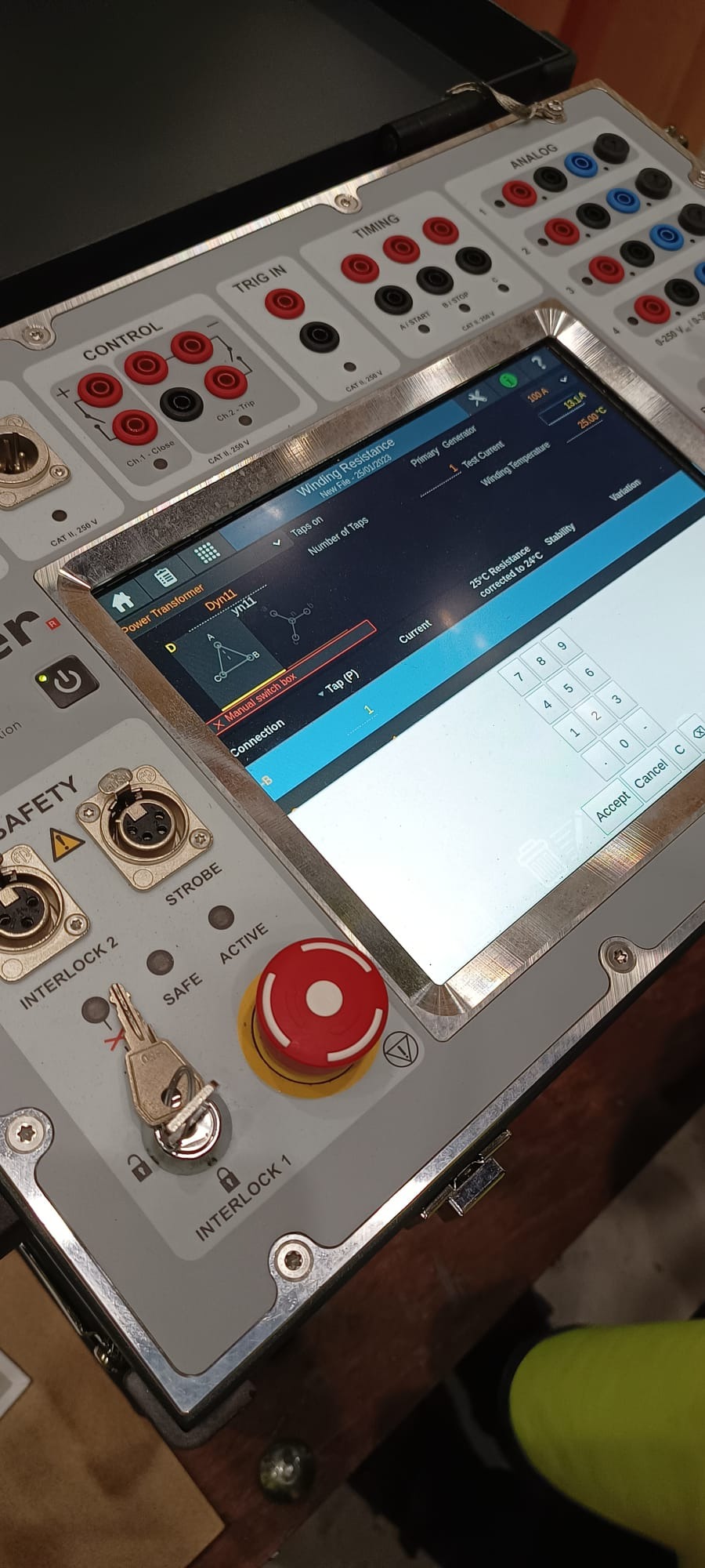 Panel sterowania urządzenia pomiarowego z ekranem dotykowym prezentującym dane o rezystancji uzwojenia transformatora, widoczne gniazda pomiarowe, przycisk bezpieczeństwa i kluczyk interlock