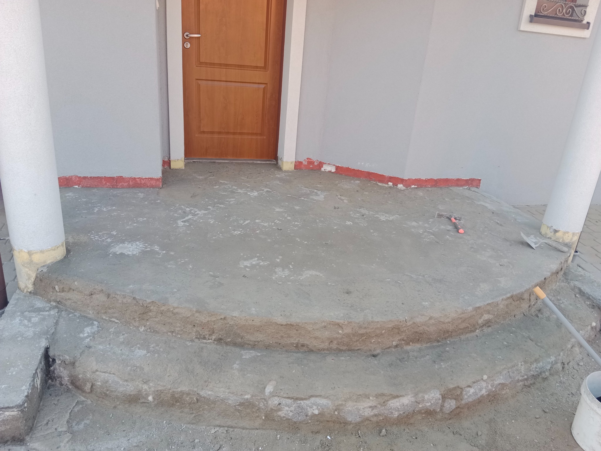 Przygotowanie podłoża pod płytki na schodach wejściowych do domu, widoczne narzędzia i wiadro. Schody w stanie surowym, przed położeniem płytek.