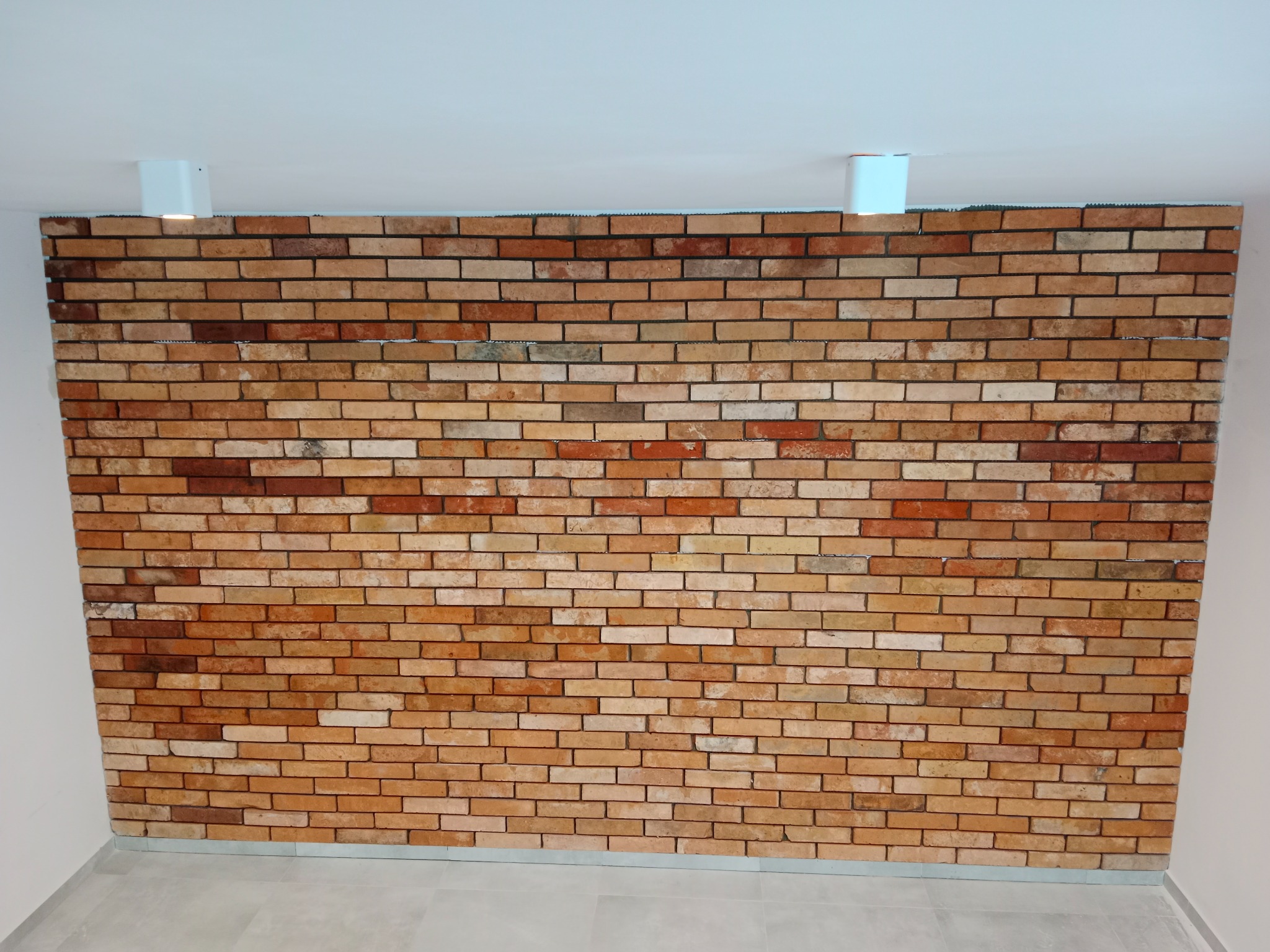 Ściana z cegły klinkierowej w Wejherowie, z dwoma nowoczesnymi lampami sufitowymi, widok z dołu.